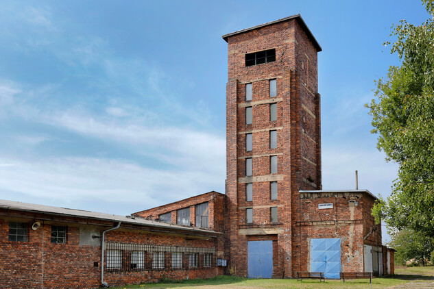 Srpen 2025 pohled na věž ve směru od východu, zamřížovaná okna jsou na kancelářích a laboratořích, kde civilní zaměstnanci zapisovali váhu každého barelu a informace o U rudě