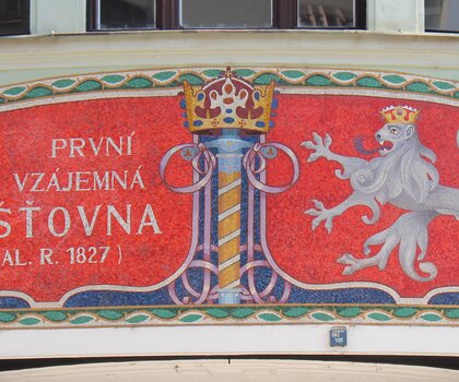 Skleněná mozaika s výrazným nápisovým polem a státním znakem nad hlavním vchodem čp. 76 (2012)